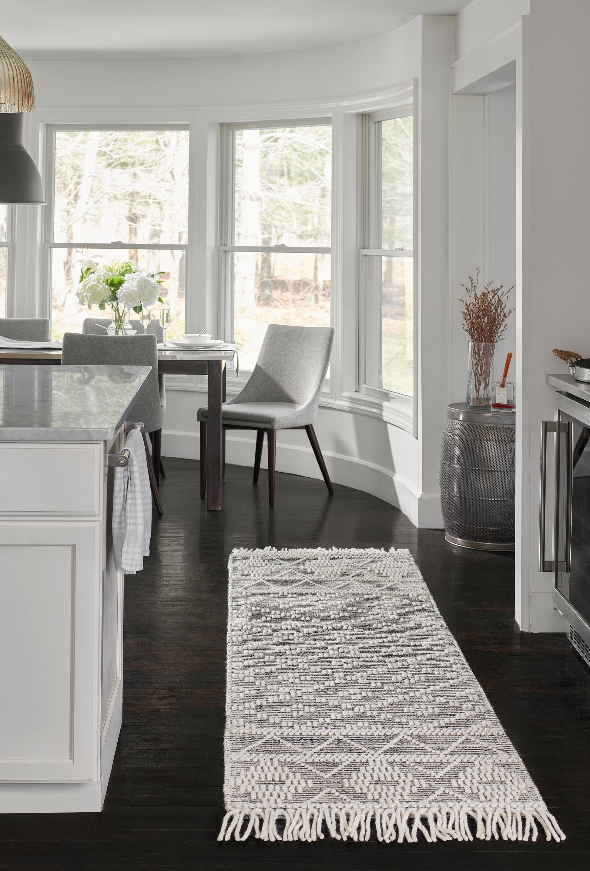 Cream and gray woven geometric area rug with fringe ends on dark hardwood kitchen floor.