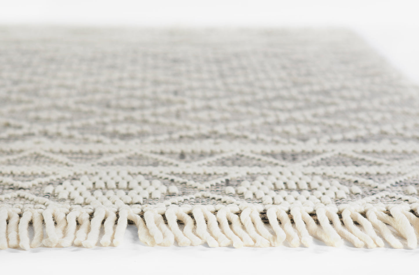 Cream and taupe geometric woven rug with cream tassel fringe along edge; soft flat-weave texture for living room decor.