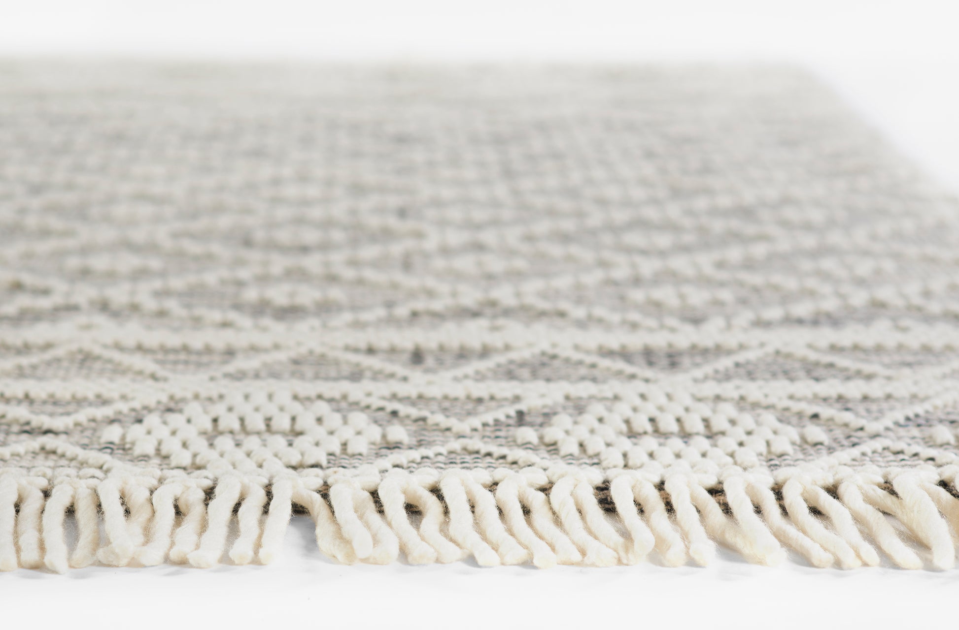 Cream and gray patterned woven rug with chunky cream fringe along edge; geometric motif, rectangular.