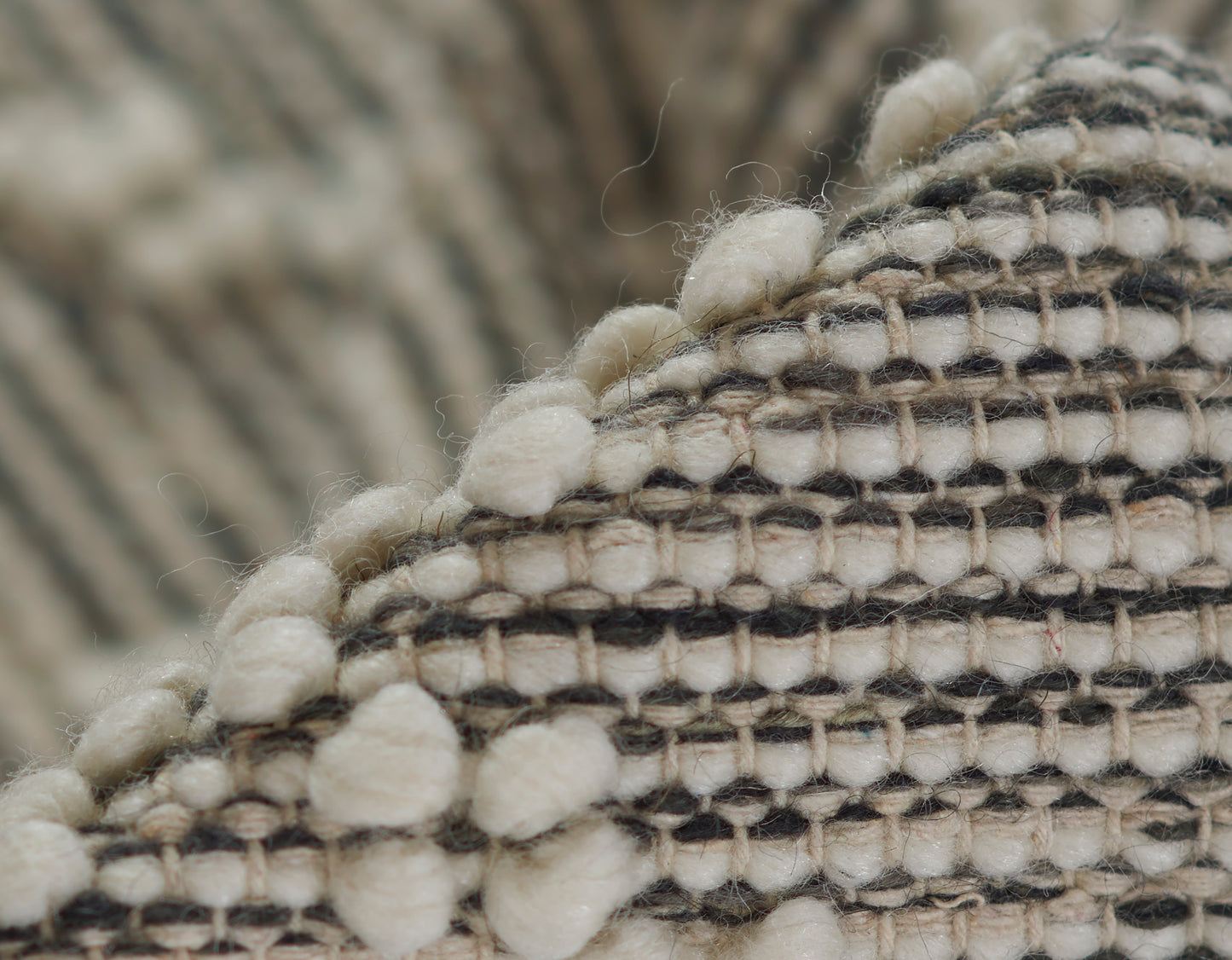 Close-up of a beige and gray striped woven rug with cream pom-pom fringe along the edge.