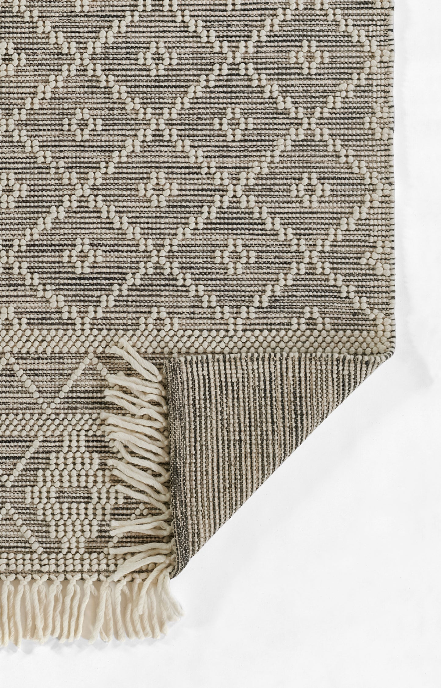 Beige and cream geometric woven rug with diamond pattern, tasseled fringe along edge and folded corner.