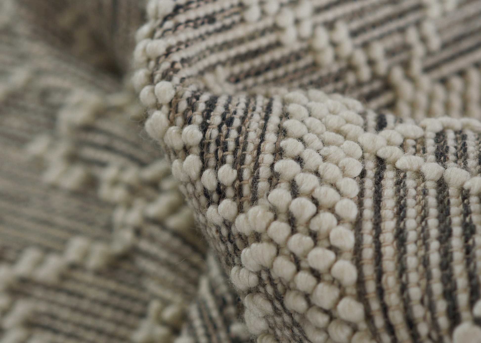 Close-up of beige charcoal boucle rug with cream pom-pom tufts and striped weave.