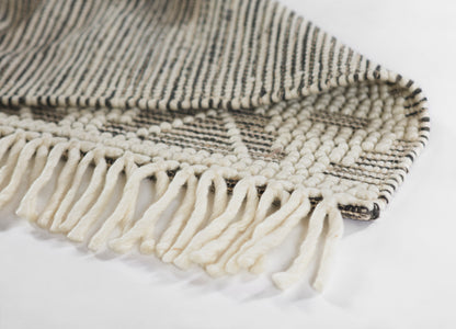 Handwoven wool rug in black and cream stripes with chunky cream fringe along the edge.