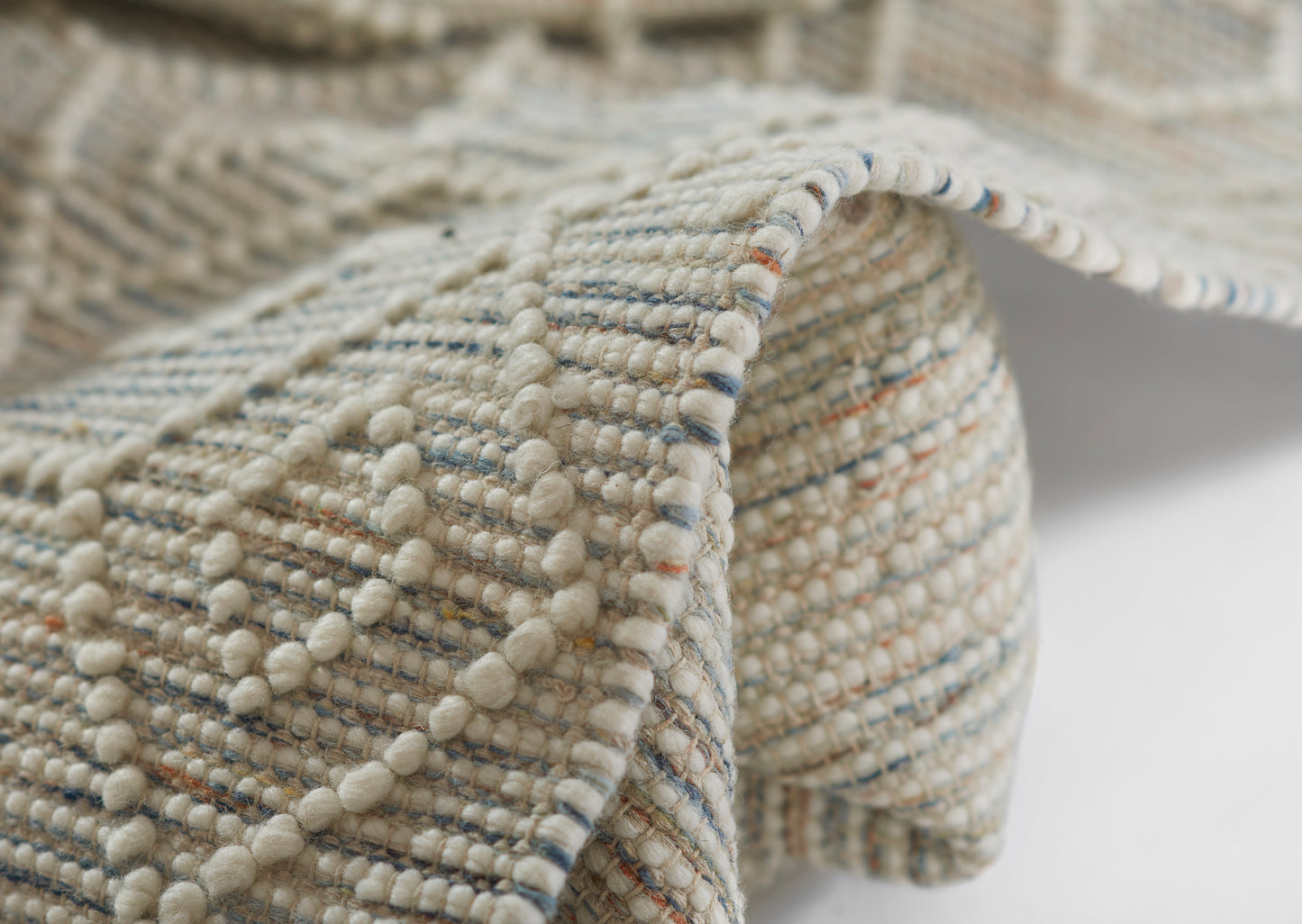 Cream boucle woven rug with looped bobbles and blue, orange, and multicolor flecks; soft, chunky texture.
