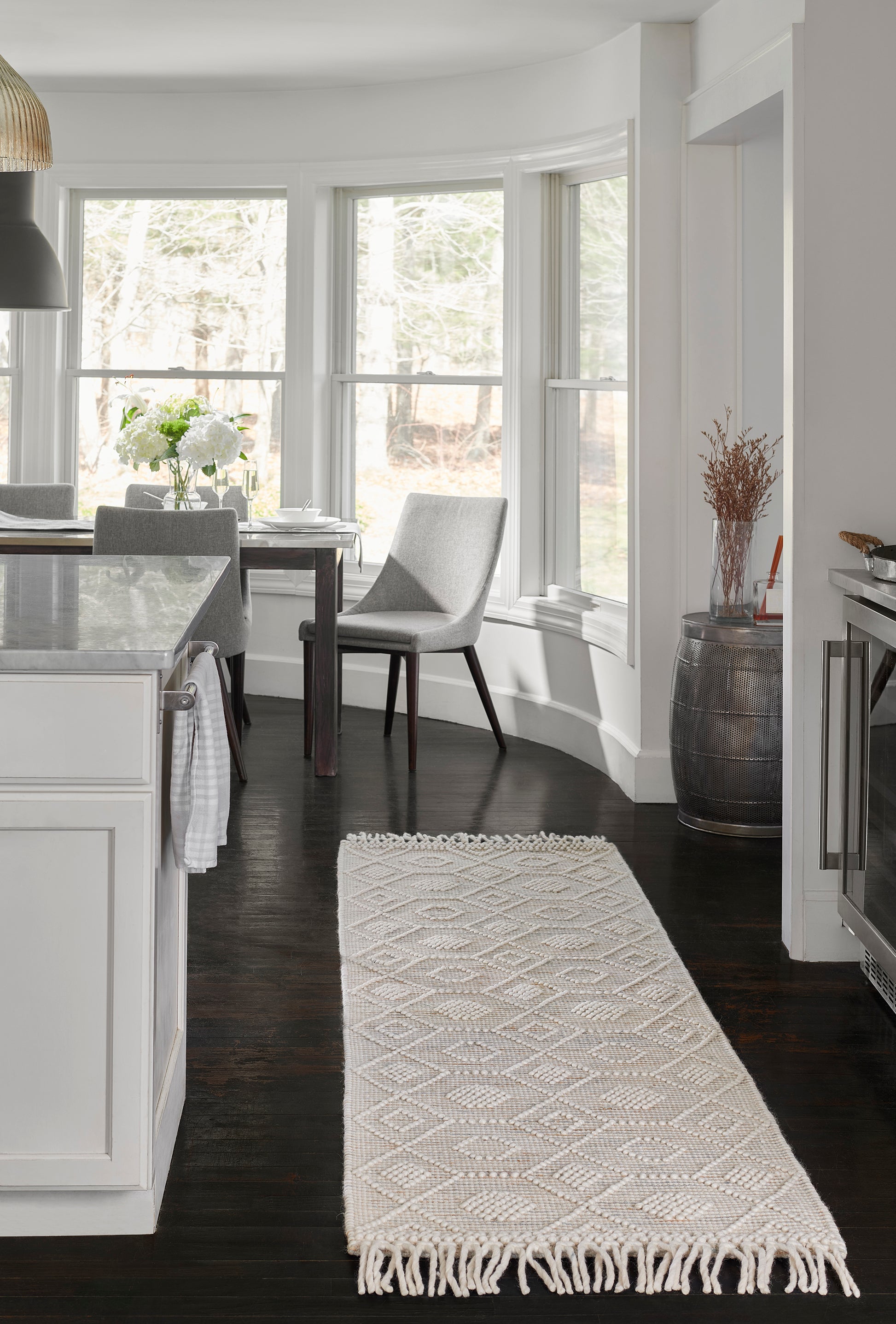 Cream woven runner rug with diamond motif and fringed ends along a dark wood floor beside a white kitchen island