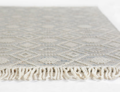 Pale blue-gray rug with ivory diamond geometric pattern and cream fringe along the edge.