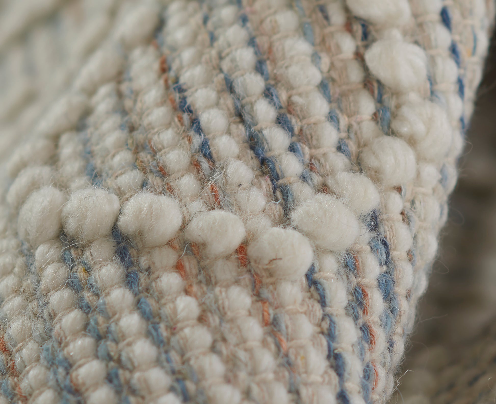 Cream boucle textile with looped yarn, ivory pom-pom textures and blue and orange stripe accents, cozy woven fabric.