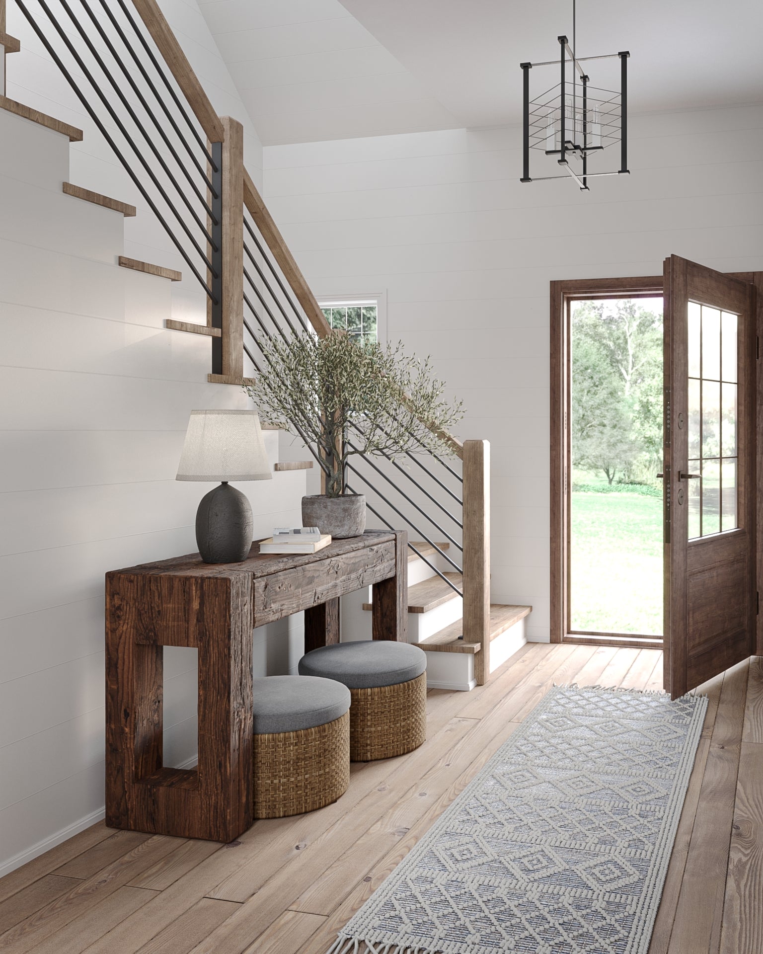 Rustic entryway with a rough wood console, two woven ottomans, a lamp, plant, staircase, glass door, and a pale patterned area rug.