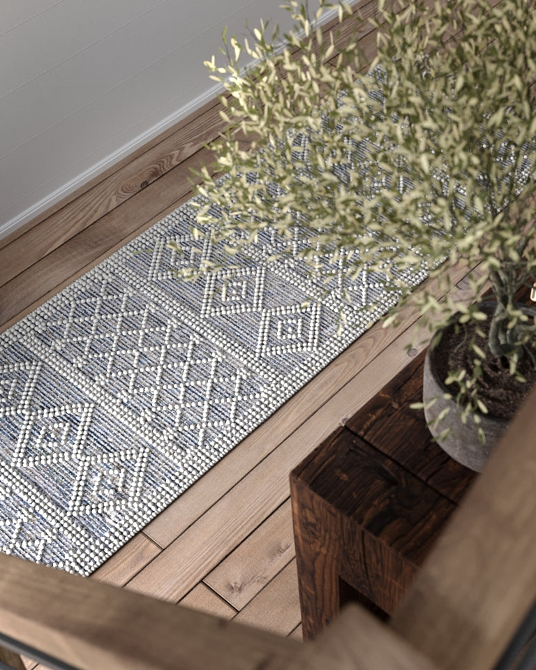 Geometric blue and white 2' x 8' rug runner on a wooden floor beside a potted plant; modern coastal style.