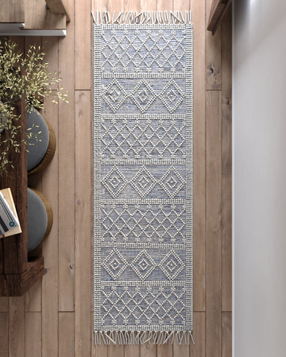 Long blue and ivory geometric woven area rug with fringe on wooden floor.