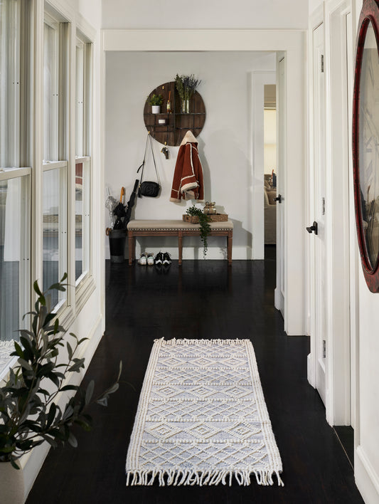 Blue-and-white geometric woven runner rug with fringe on a dark hardwood hallway.