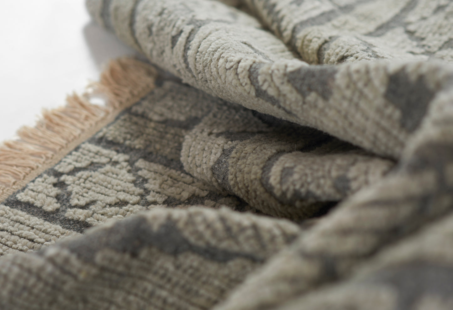 Close-up of a gray and beige patterned rug with soft pile and tan fringe.