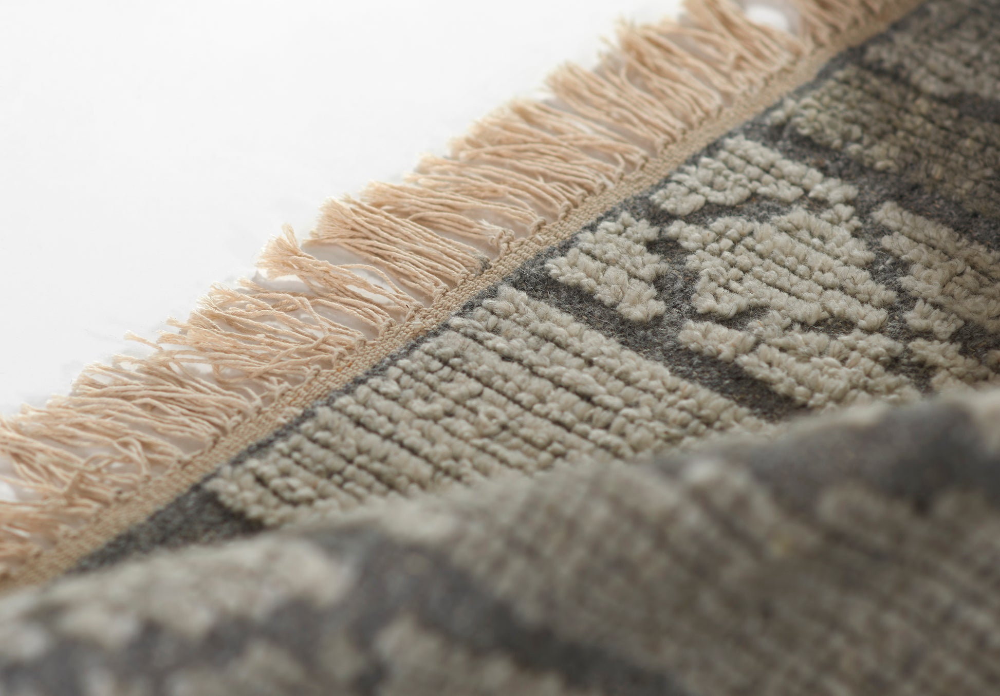 Beige fringe along edge of a grey and cream geometric rug with a textured wool pile.