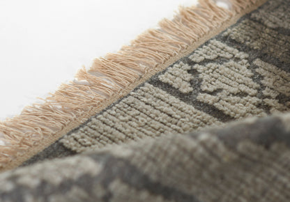 Beige fringe edge on a gray geometric rug with cream and charcoal pattern; textured and decorative.