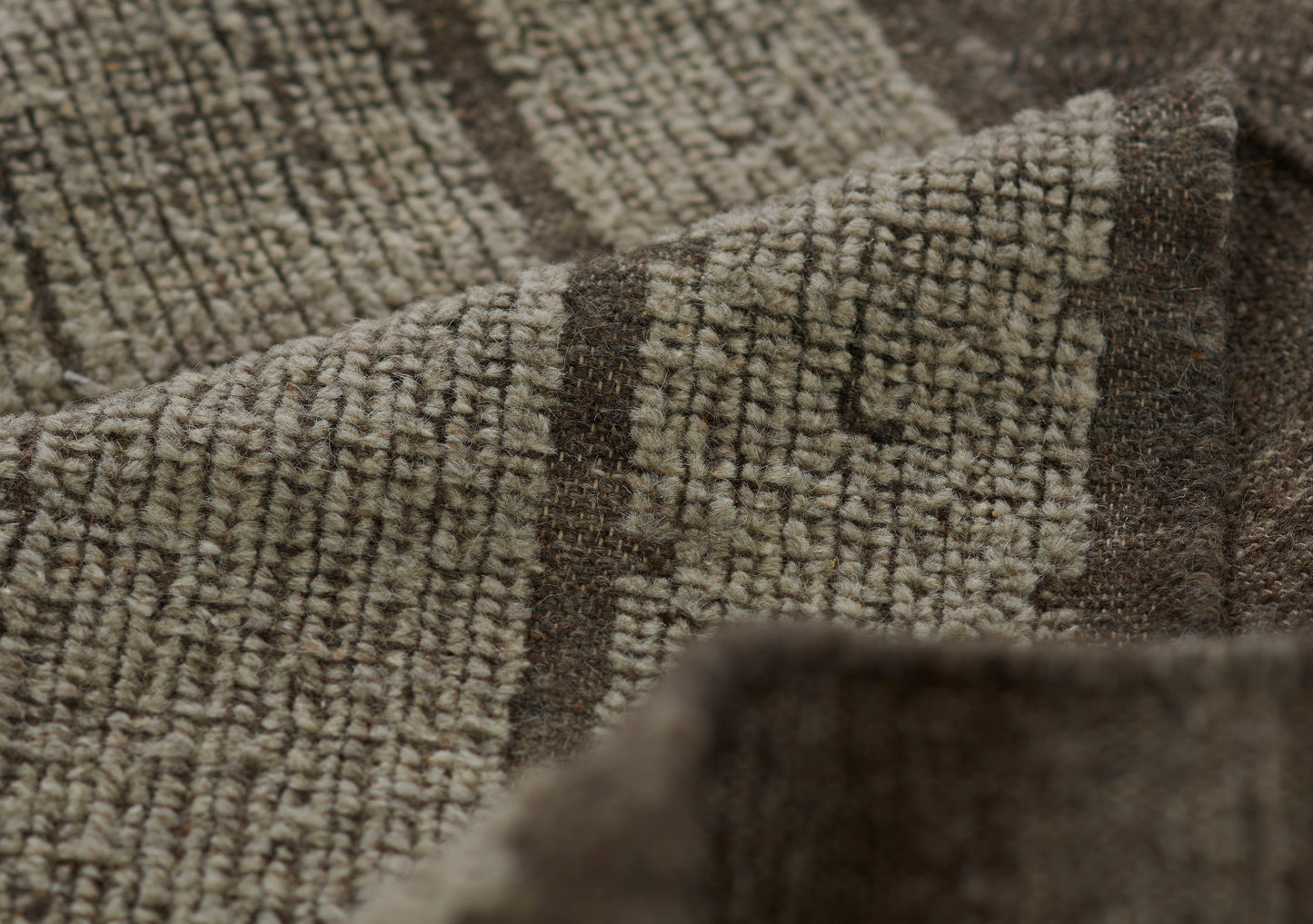 Close-up of a brown and beige woven rug with geometric block pattern and soft textured pile.