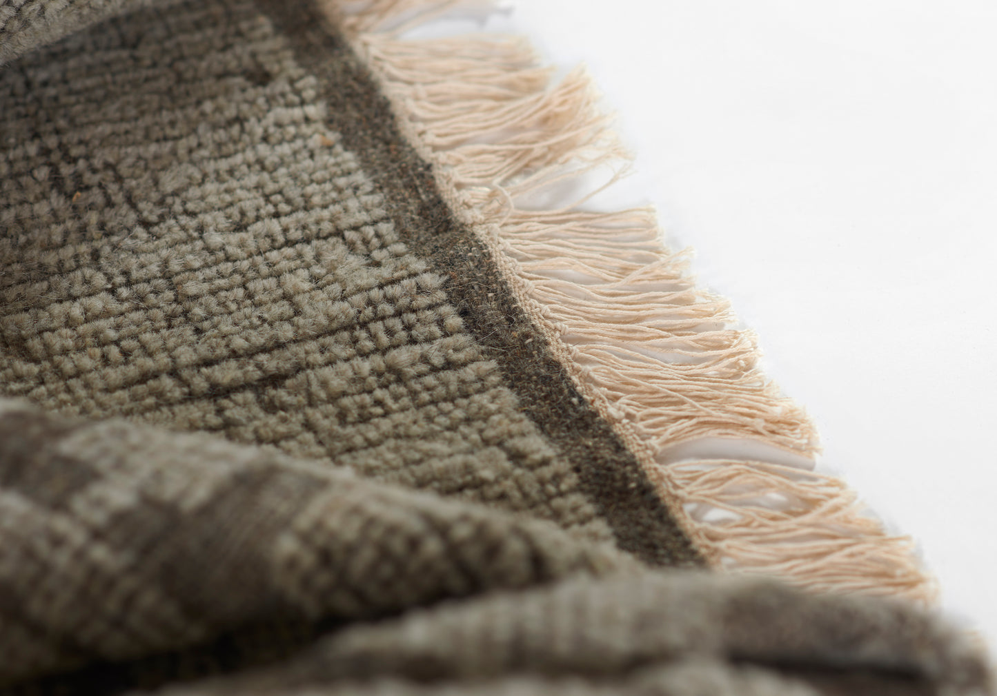 Close-up of a textured woven rug in taupe and brown tones with natural beige fringe along edge.