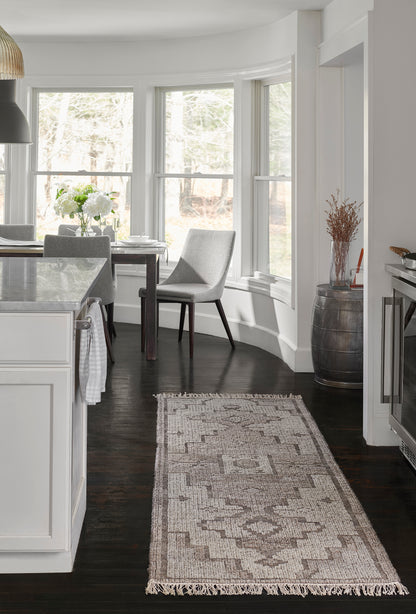 Natural-toned geometric runner rug with fringed ends on dark hardwood, in a modern white kitchen & gray upholstered chairs.