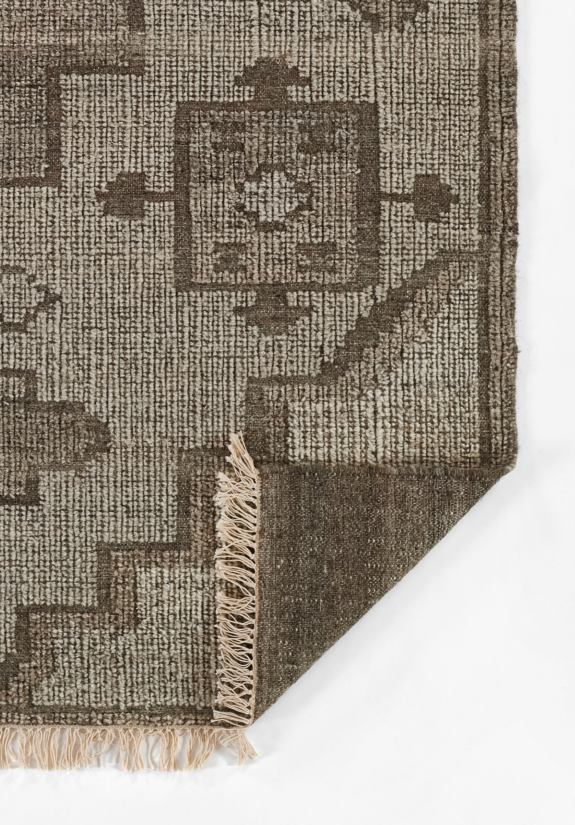 Brown and tan geometric woven rug with central medallion, bordered pattern, fringed edge, folded corner.