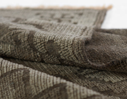 Brown and beige woven rug with textured loop pile, geometric pattern, fringed edge; natural earthy tones.