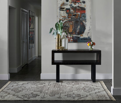 Dark wood console table with gold vase, glass bottle, leafy plant, abstract painting & beige geometric rug.