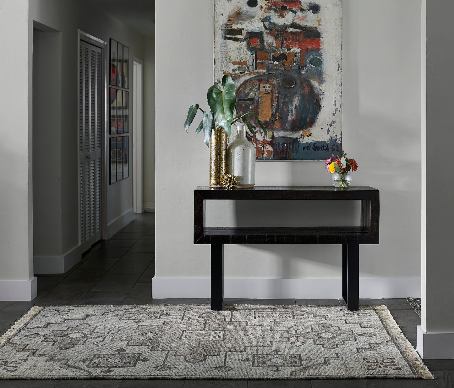 Black modern console table with gold and glass vases, green plant, abstract art above, beige patterned rug.