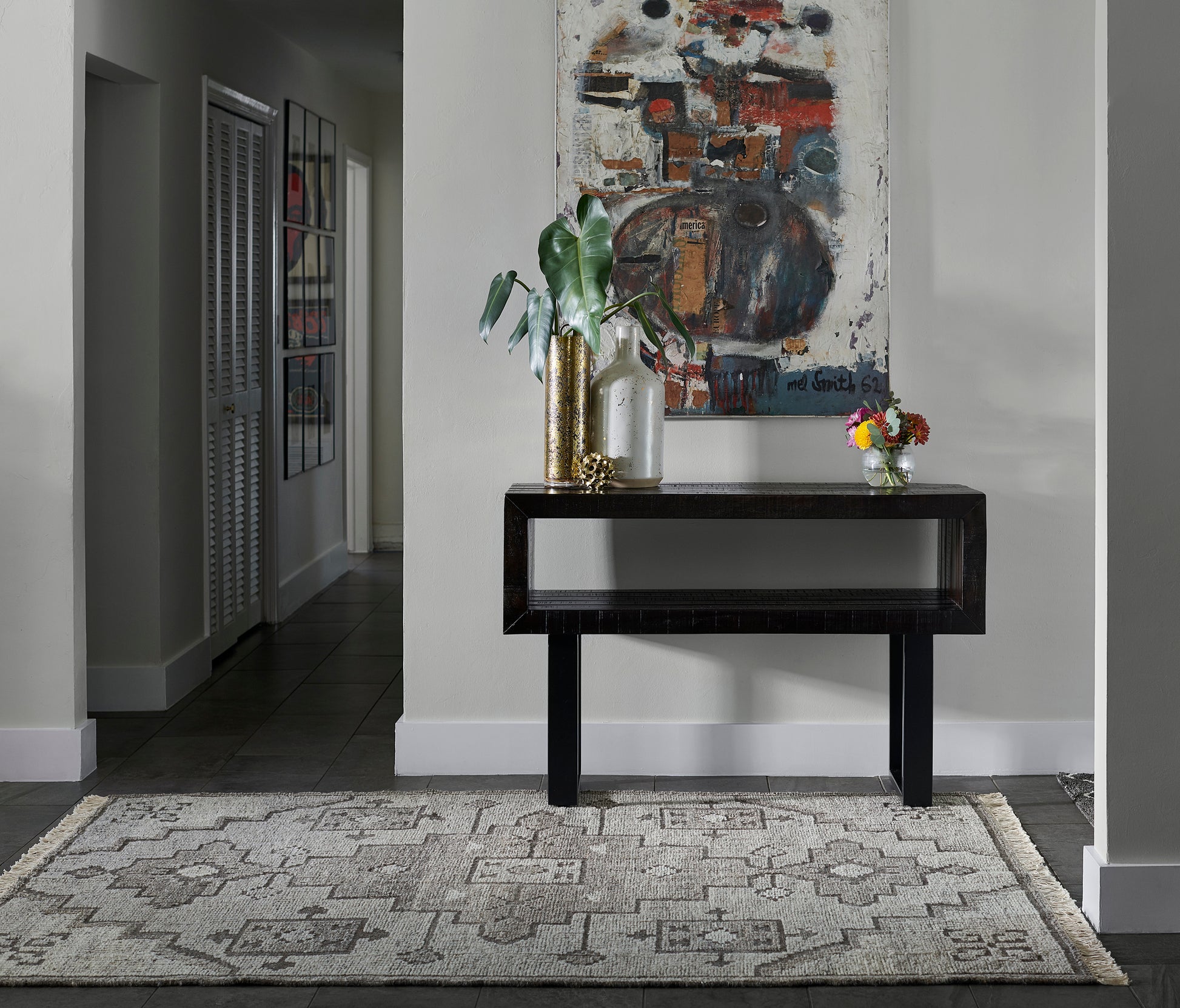 Black modern console table with gold and glass vases, green plant, abstract art above, beige patterned rug.