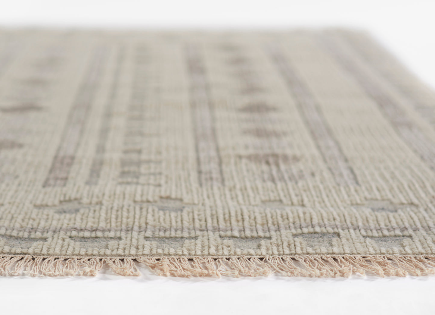 Ivory-beige woven rug with subtle taupe geometric pattern and fringe edge, soft textured indoor decor.