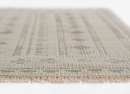Ivory beige woven rug with subtle geometric pattern and pink-tan fringe along edge.