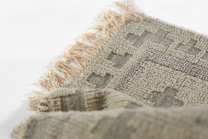 Neutral woven rug with geometric taupe, ivory and gray pattern and fringed ends.