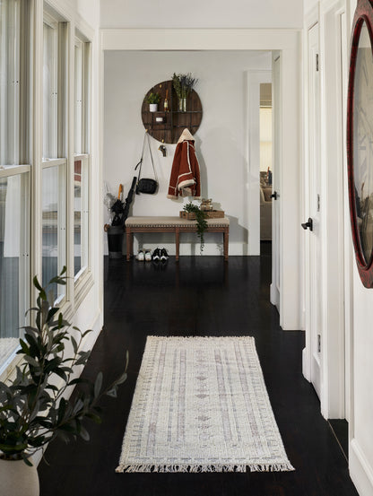 Cream woven runner rug with fringe on a dark hardwood hallway, flanked by windows and a cozy entryway bench.