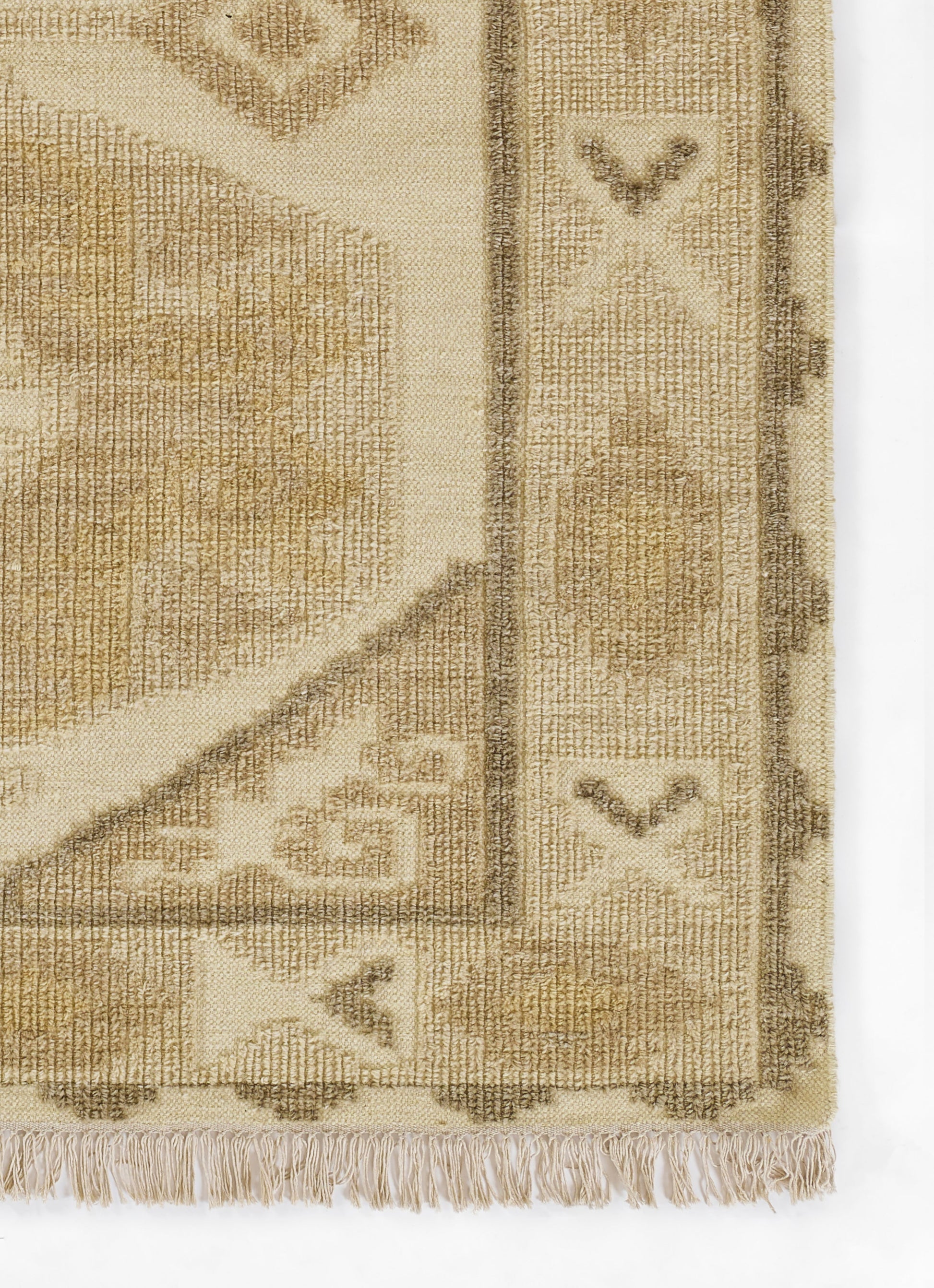 Rectangular beige-tan rug with woven texture, geometric border motifs and fringe along bottom edge.