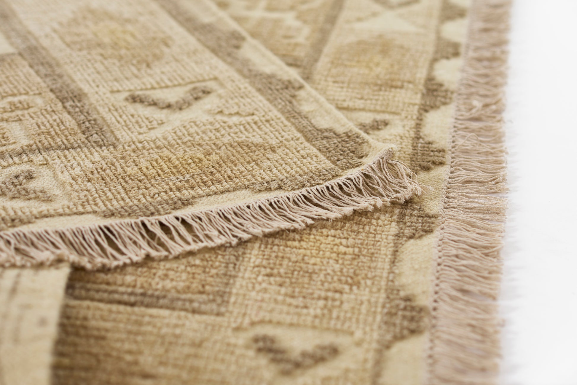 Beige geometric rug with tassel fringe along edges; woven texture in natural neutral tones.