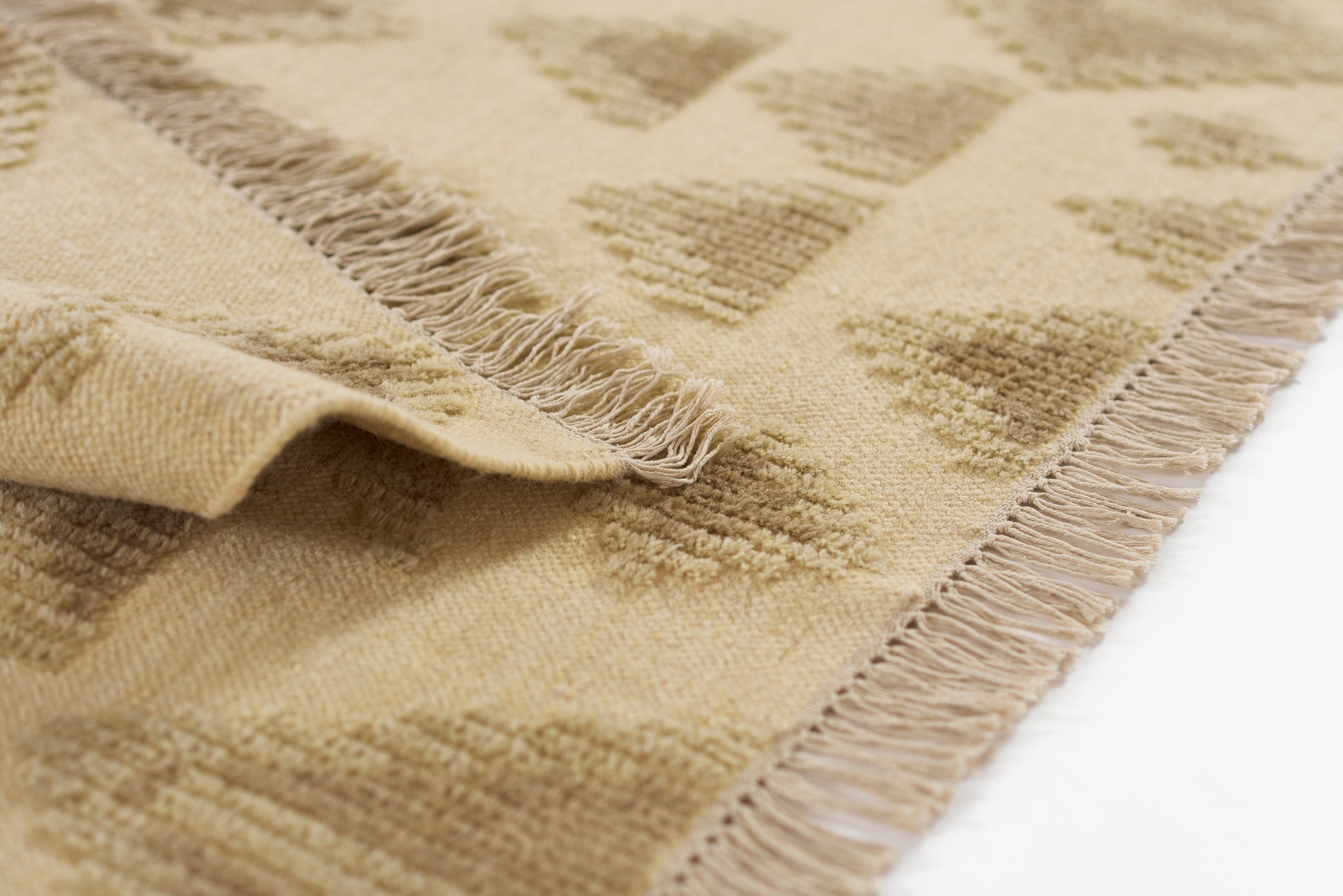 Beige woven rug with tan geometric pattern and short fringe along edges; natural fiber texture, soft and warm.