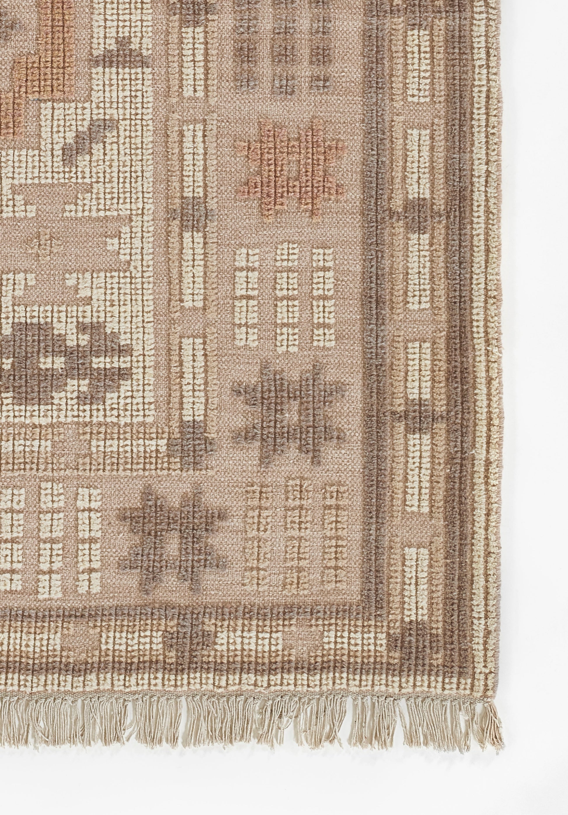Beige-brown patterned rug with geometric motifs and tassel fringe along the edge.