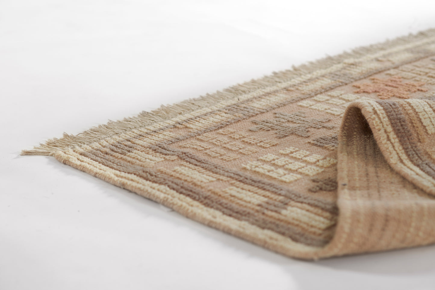 Beige & brown geometric area rug with cream accents & fringed edge, folded at the corner.
