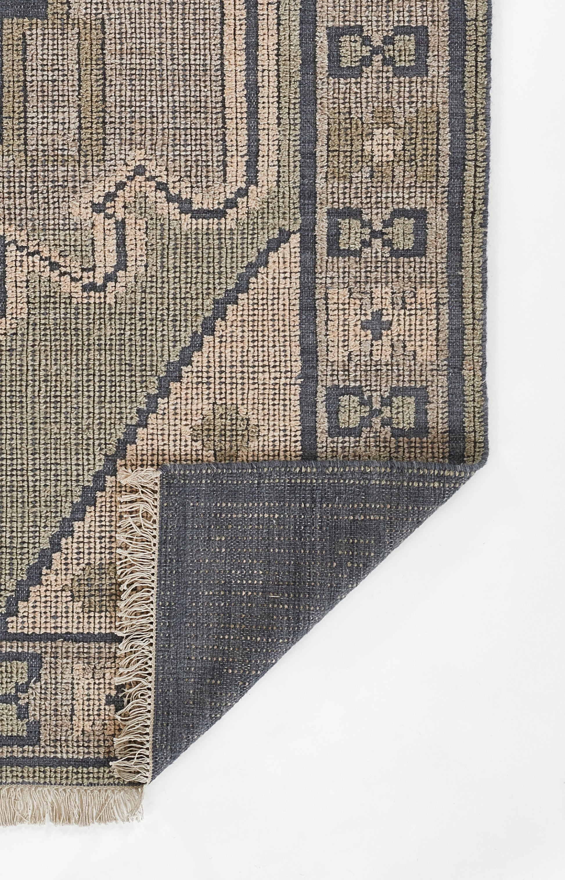 Beige & navy woven rug with geometric border & small motifs; fringed edge, corner folded to show underside.