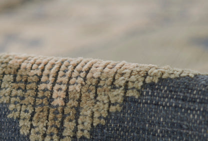 Close-up of beige-tan woven rug edge with textured pile against dark blue fabric.