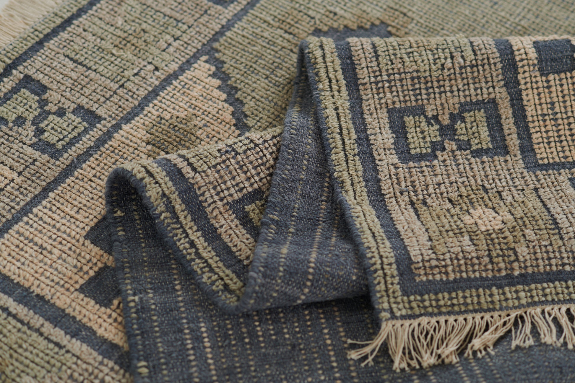 Blue and beige geometric woven rug with fringe edges; folded corner reveals kilim-style pattern.