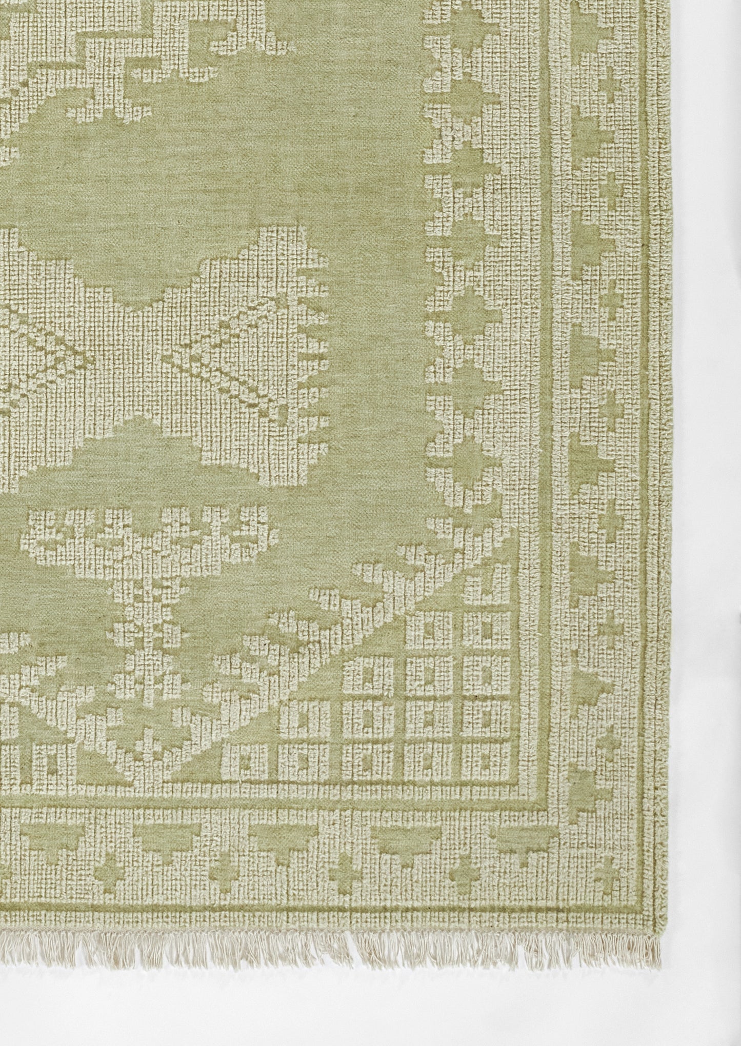 Rectangular sage-green woven rug with light geometric border and fringe; traditional floor decor.