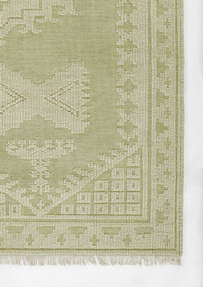 Rectangular sage-green woven rug with light geometric border and fringe; traditional floor decor.