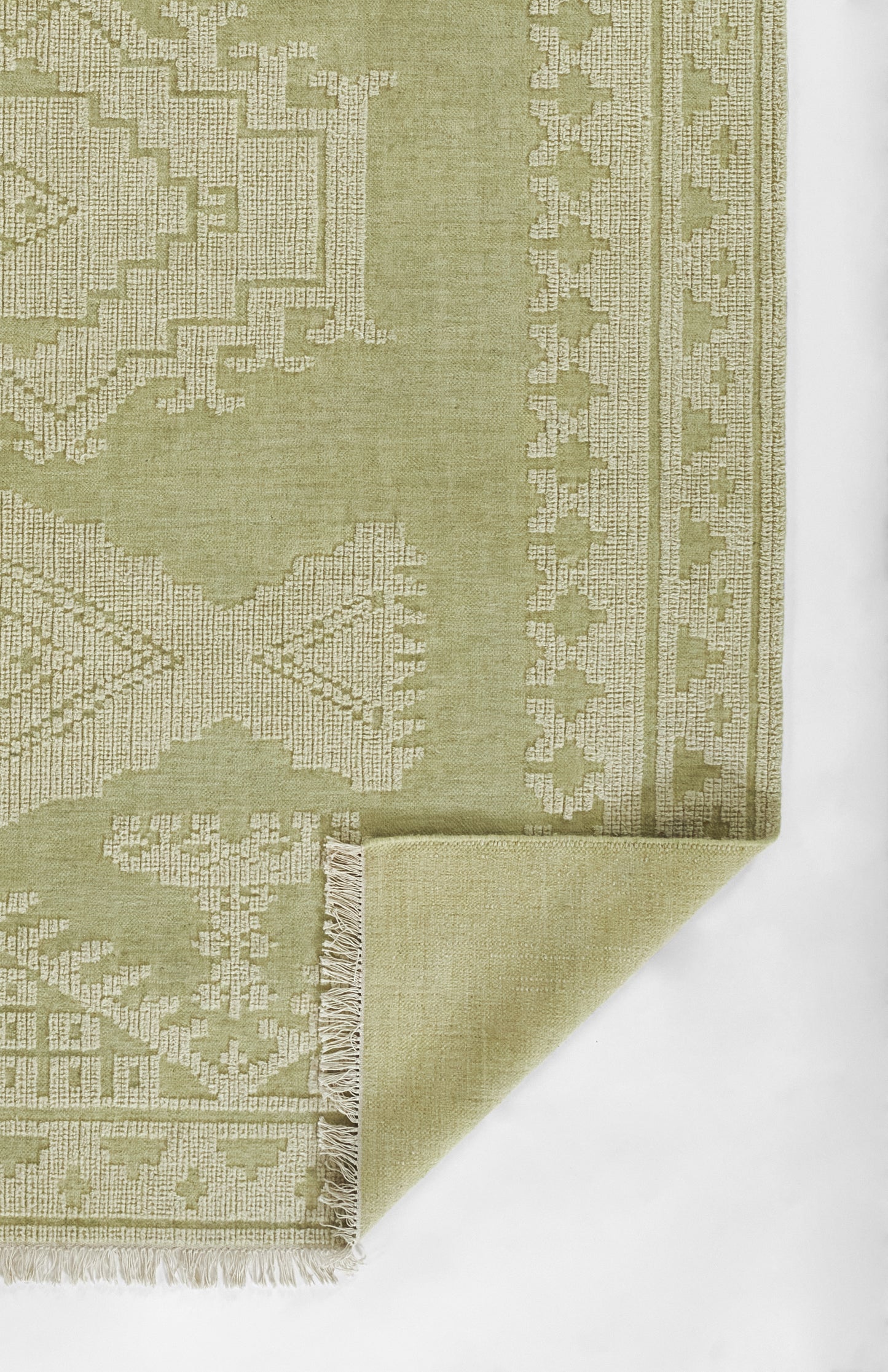 Olive green geometric woven rug with beige pattern, fringed edge, folded corner.