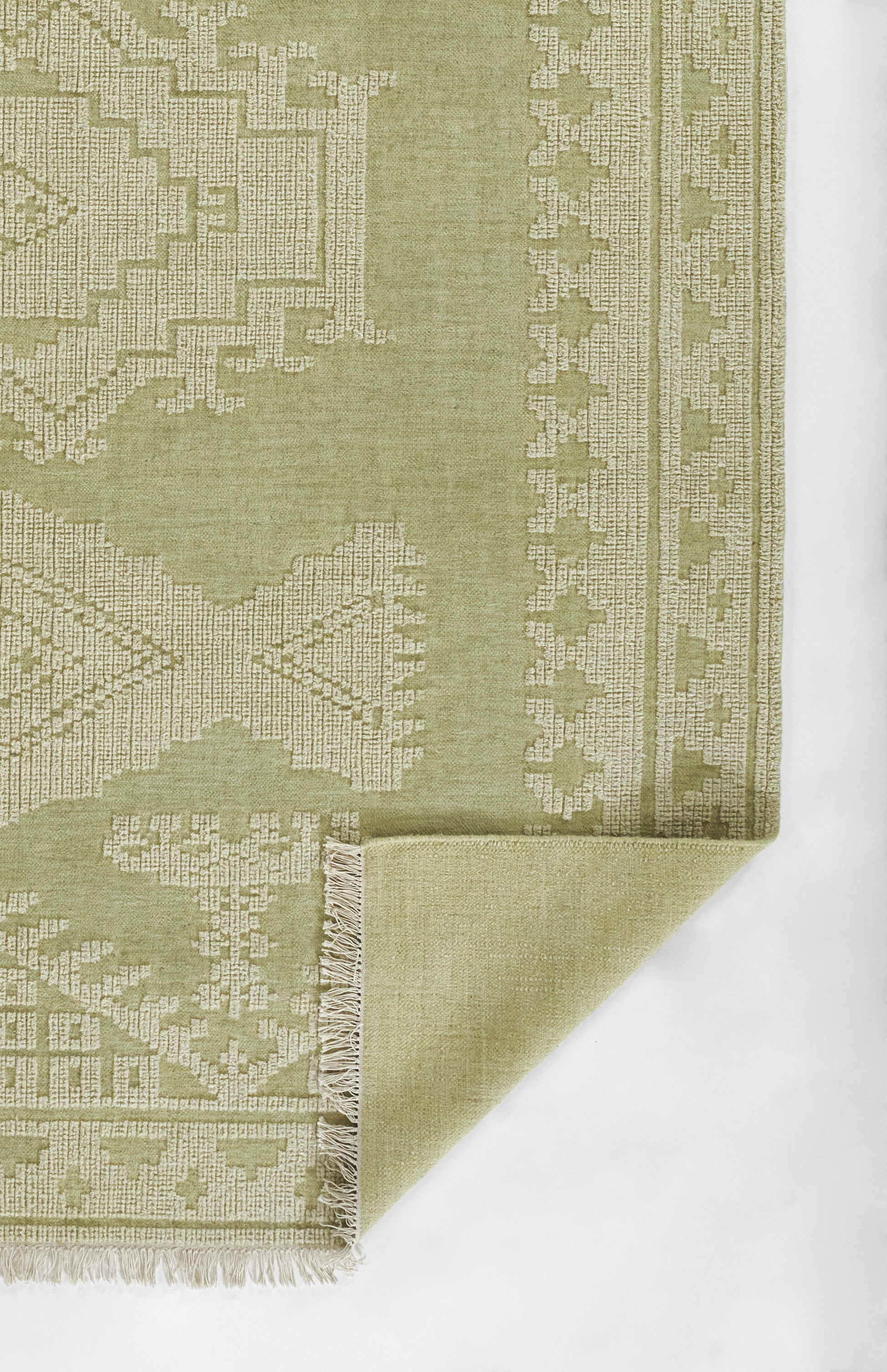 Olive green geometric woven rug with beige pattern, fringed edge, folded corner.