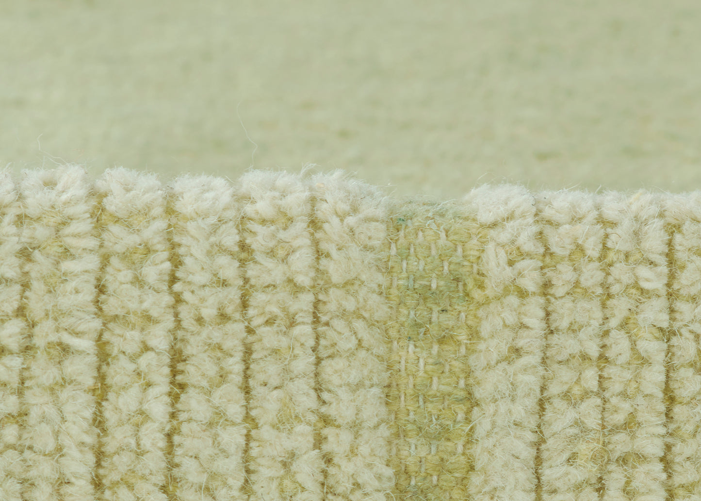Close-up of pale green looped rug edge with cream fibers and ribbed texture.