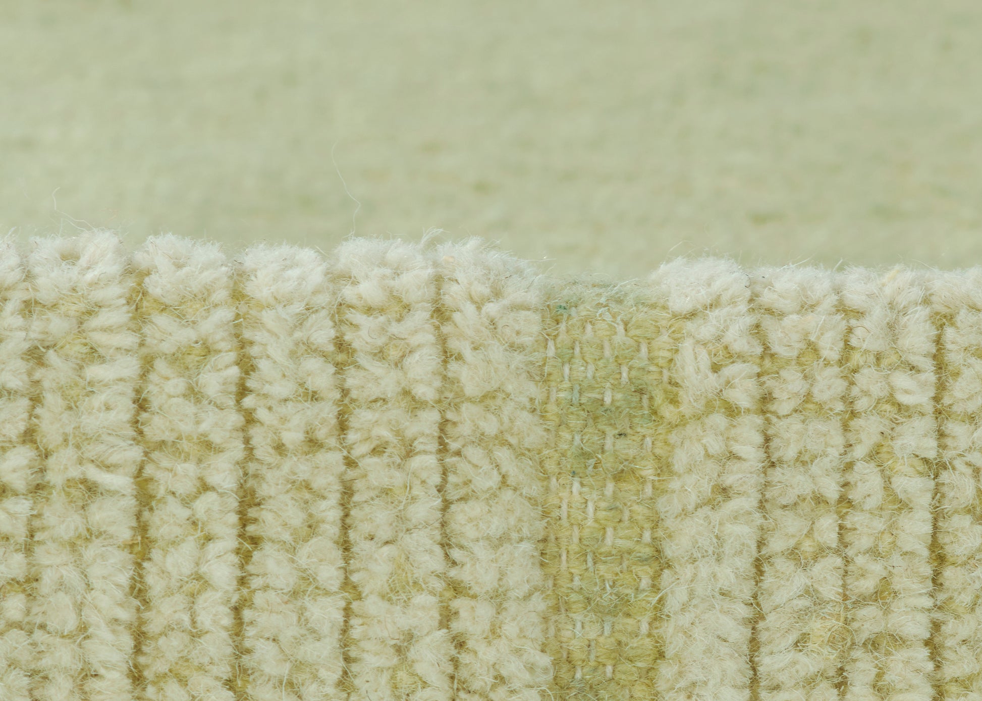 Close-up of pale green looped rug edge with cream fibers and ribbed texture.
