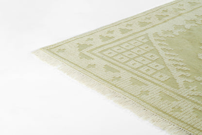 Sage green area rug with cream lattice and diamond motifs, fringed edges.