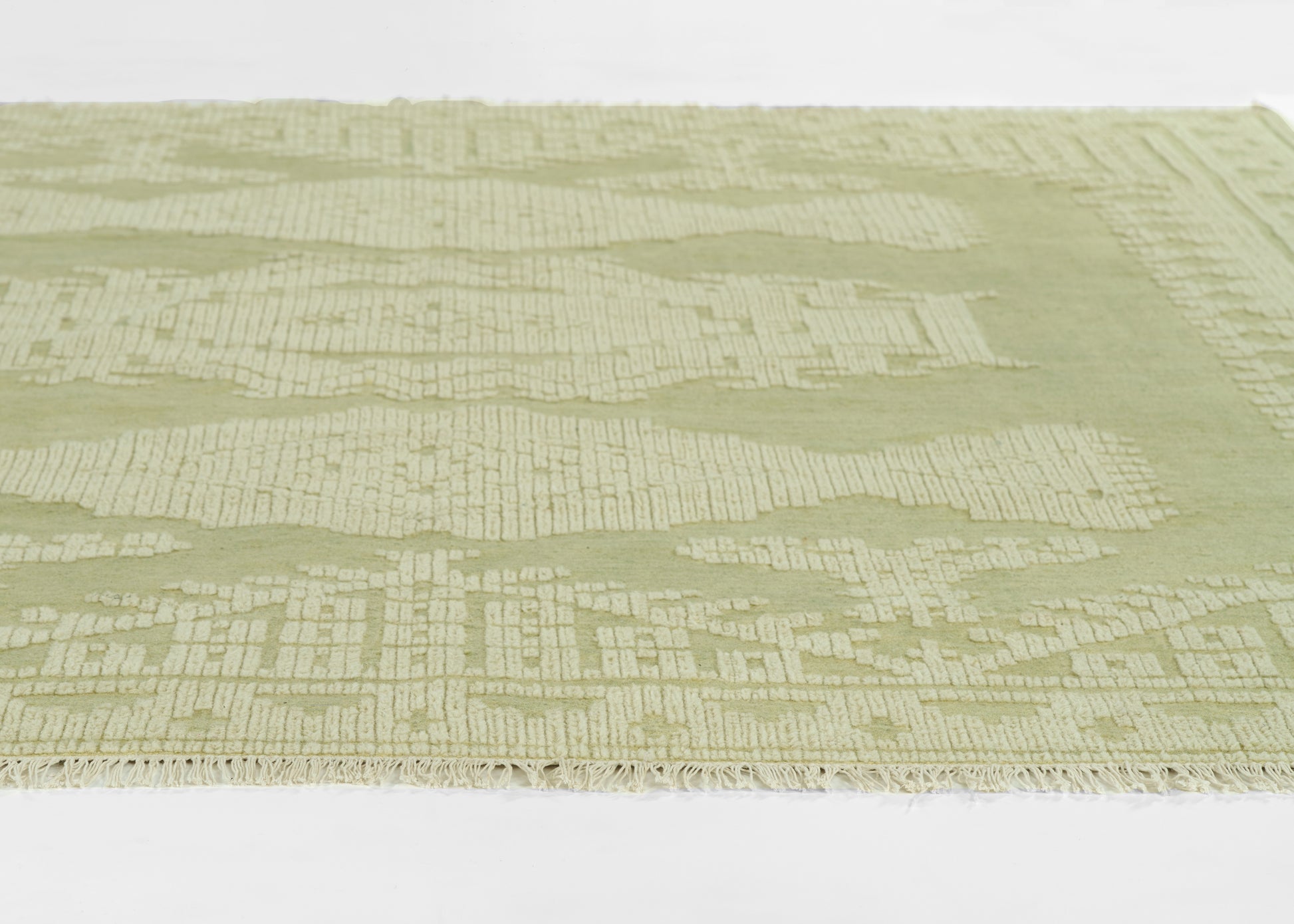 Sage-green rug with subtle cream geometric pattern and fringed edge.