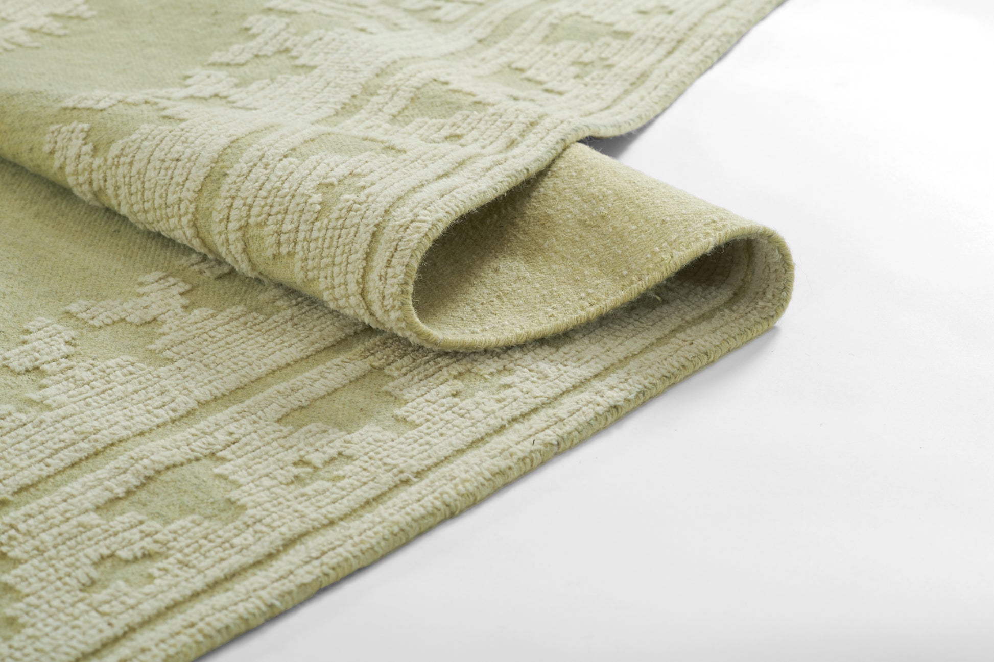 Sage-green textured rug with embossed geometric motif and rolled edge.