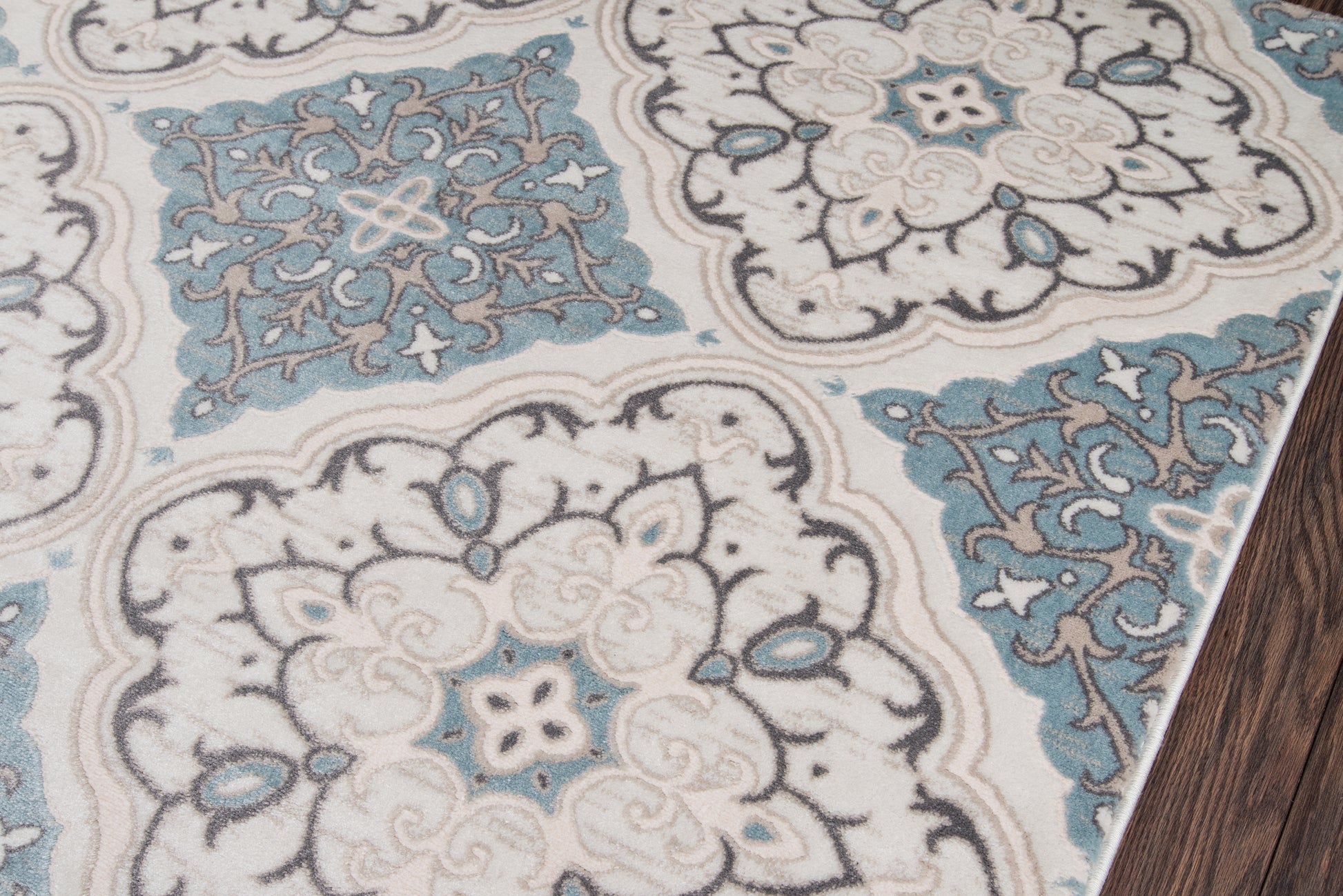 Persian-style rug with ivory and teal-blue medallions, intricate floral damask pattern on wood floor.