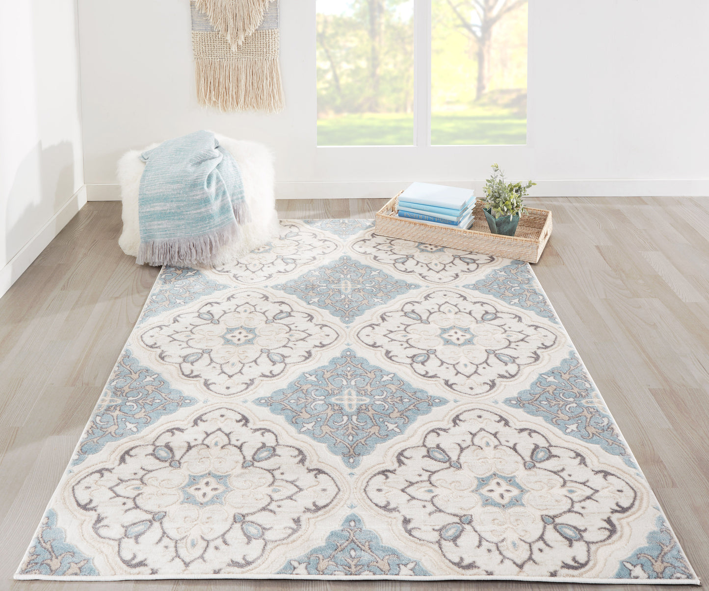 Rectangular boho area rug in ivory and pale blue with medallion pattern; cozy throw on fluffy ottoman; tray with books.
