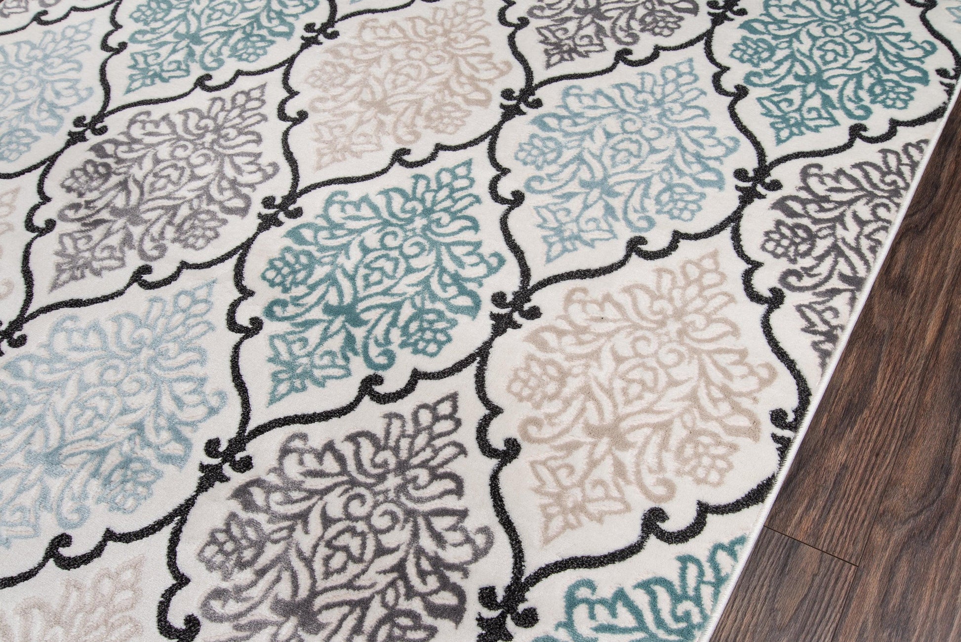 Patterned area rug with teal, beige and gray floral medallions outlined in black on a wood floor.